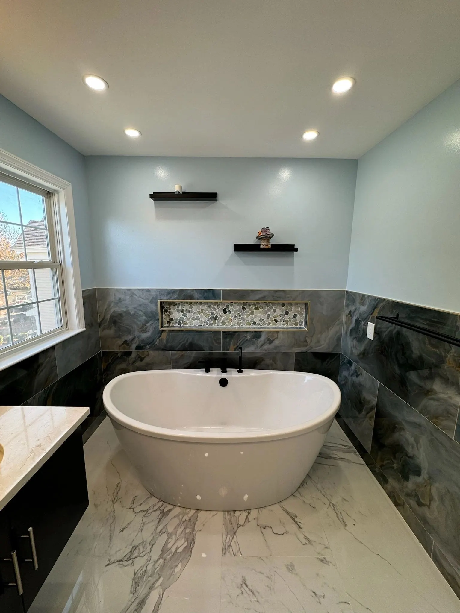 Freestanding tub on a marble-look floor under a window