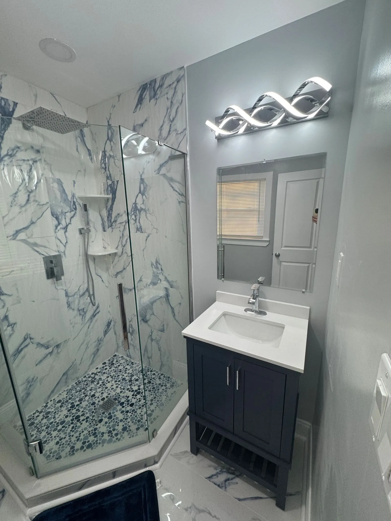 Corner glass shower with blue-veined walls and a pebble floor
